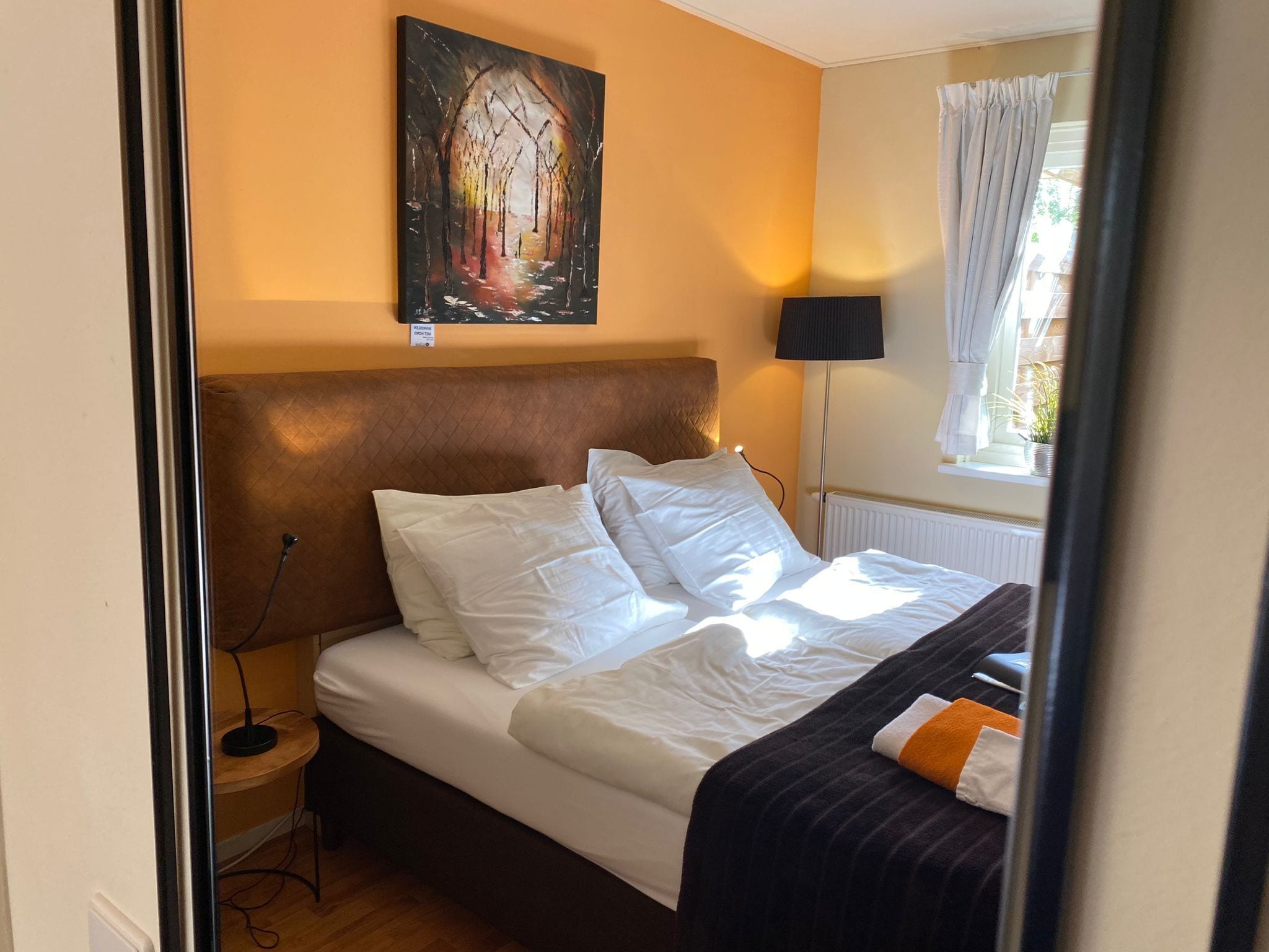 A neatly made bed with white linens, a dark headboard, and a painting above it.