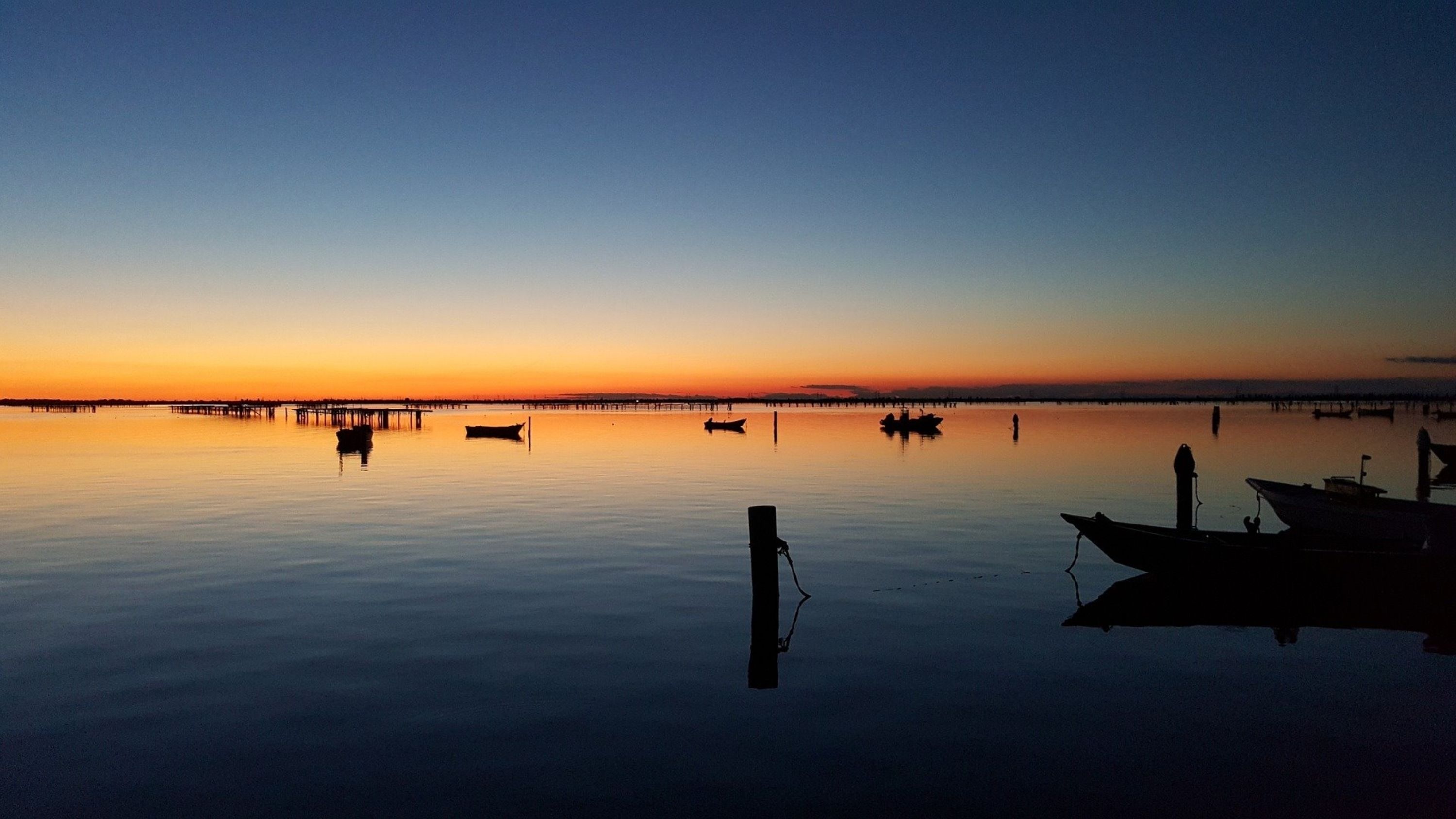 A calm waterfront at sunset with boats docked.