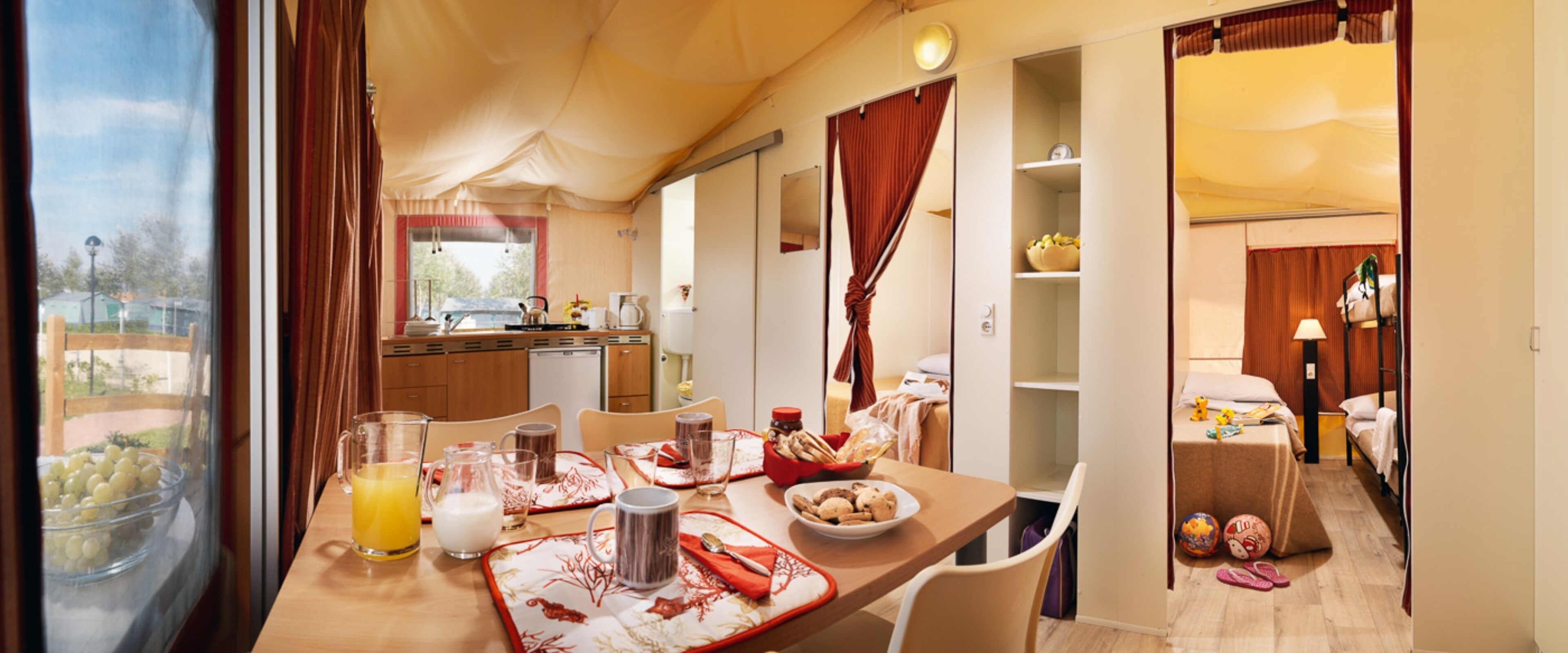 Un coin repas avec une table mise pour le petit-déjeuner, une cuisine en arrière-plan et une chambre avec un lit superposé.
