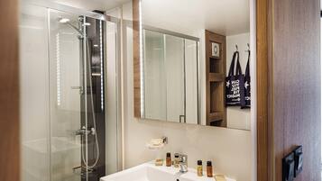 A modern bathroom with a glass-enclosed shower, a white sink with toiletries, and a mirror reflecting the room.