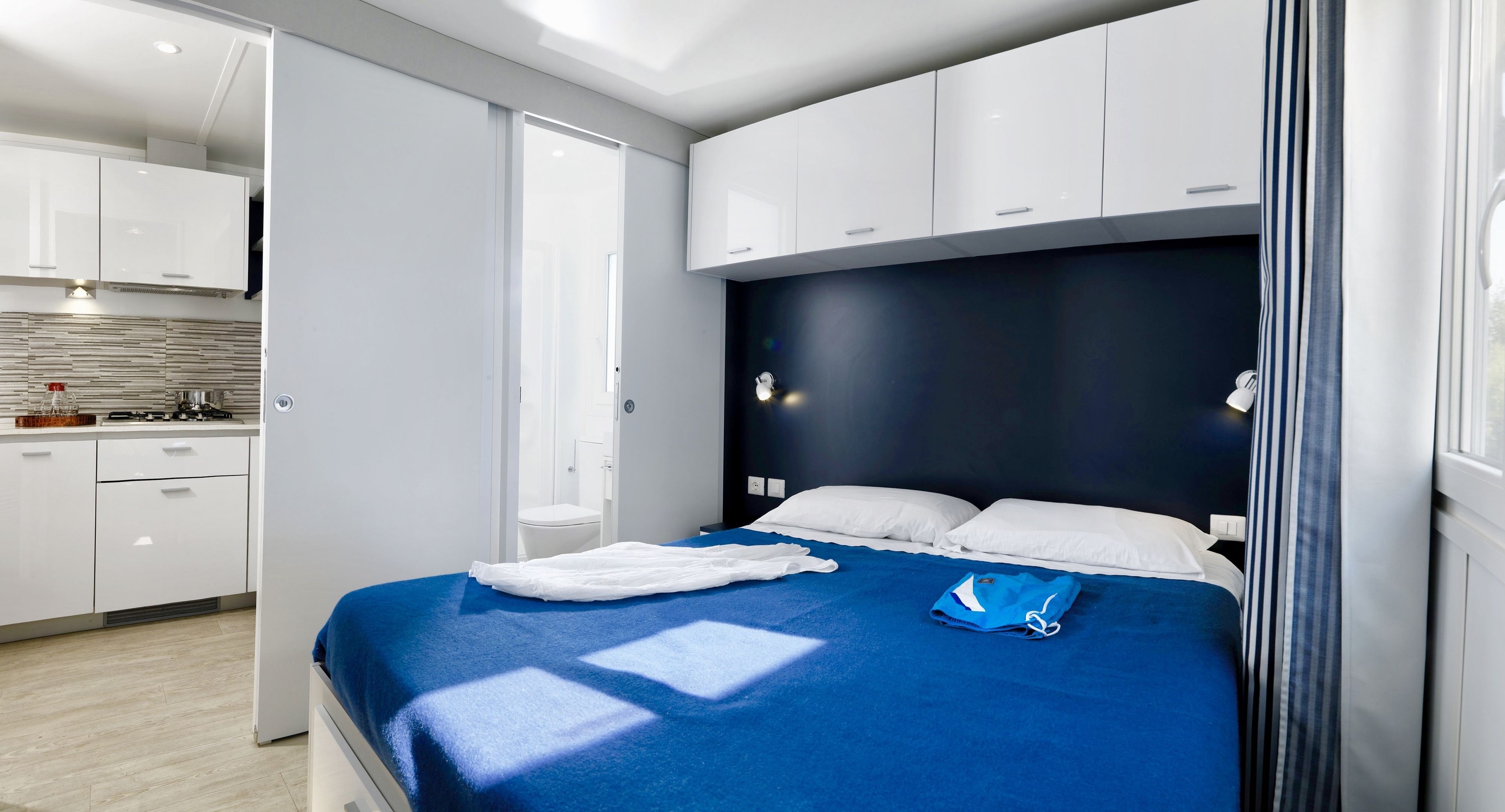 A modern hotel room with a large bed, a separate bathroom, and a kitchenette.