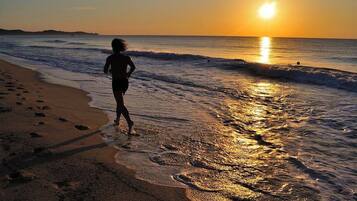 Une scène de plage où l’on voit une personne se promenant le long du rivage au coucher du soleil.