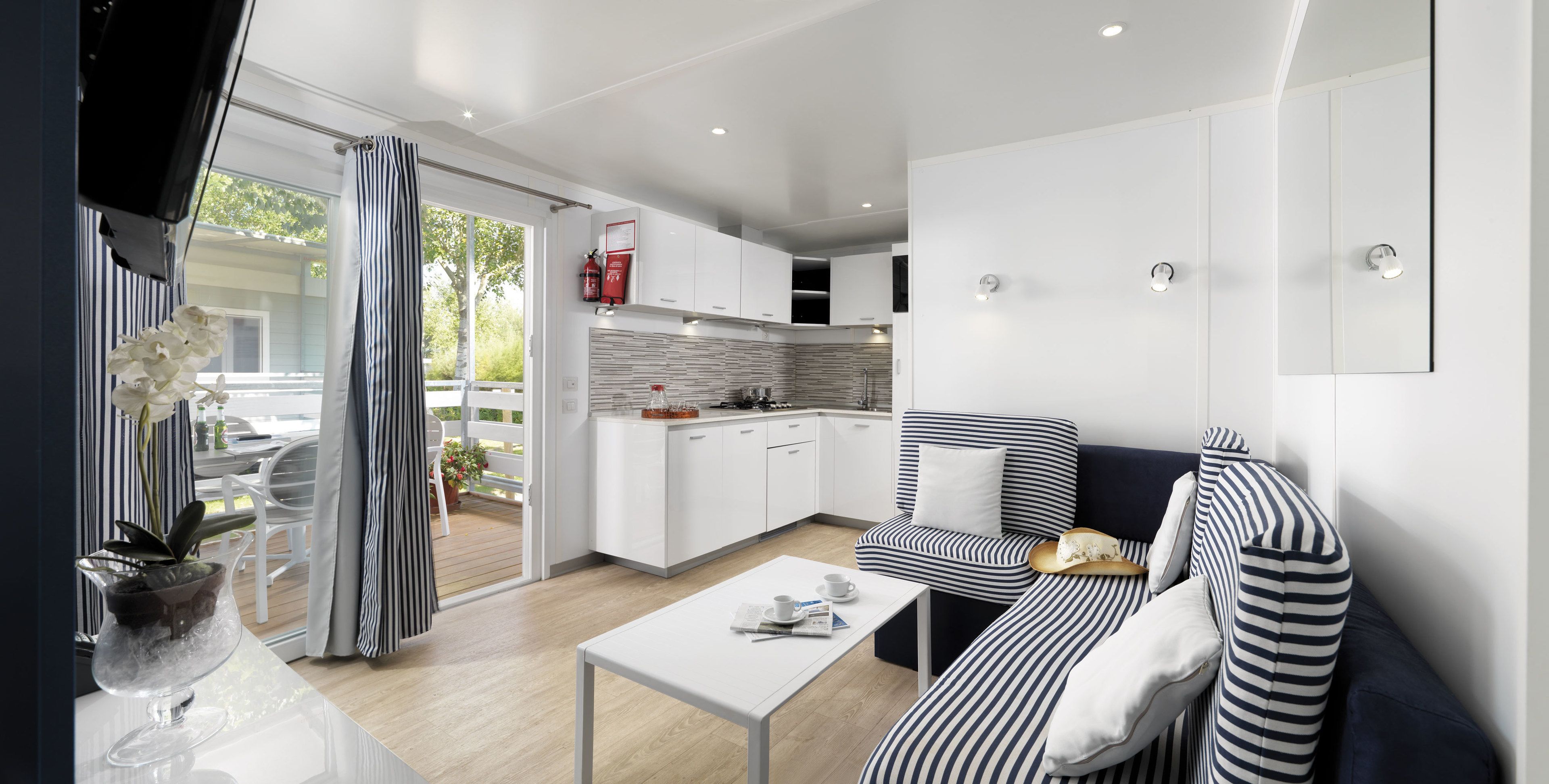 A modern kitchen with white cabinets, a striped sofa, and a dining area with a white table.