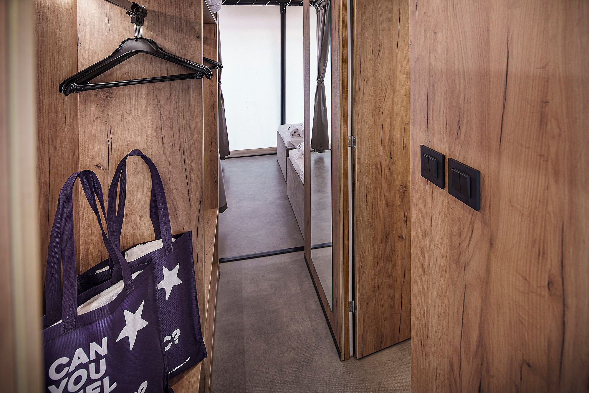 A hallway with wooden walls, a hanging bag, and a bed in the background.