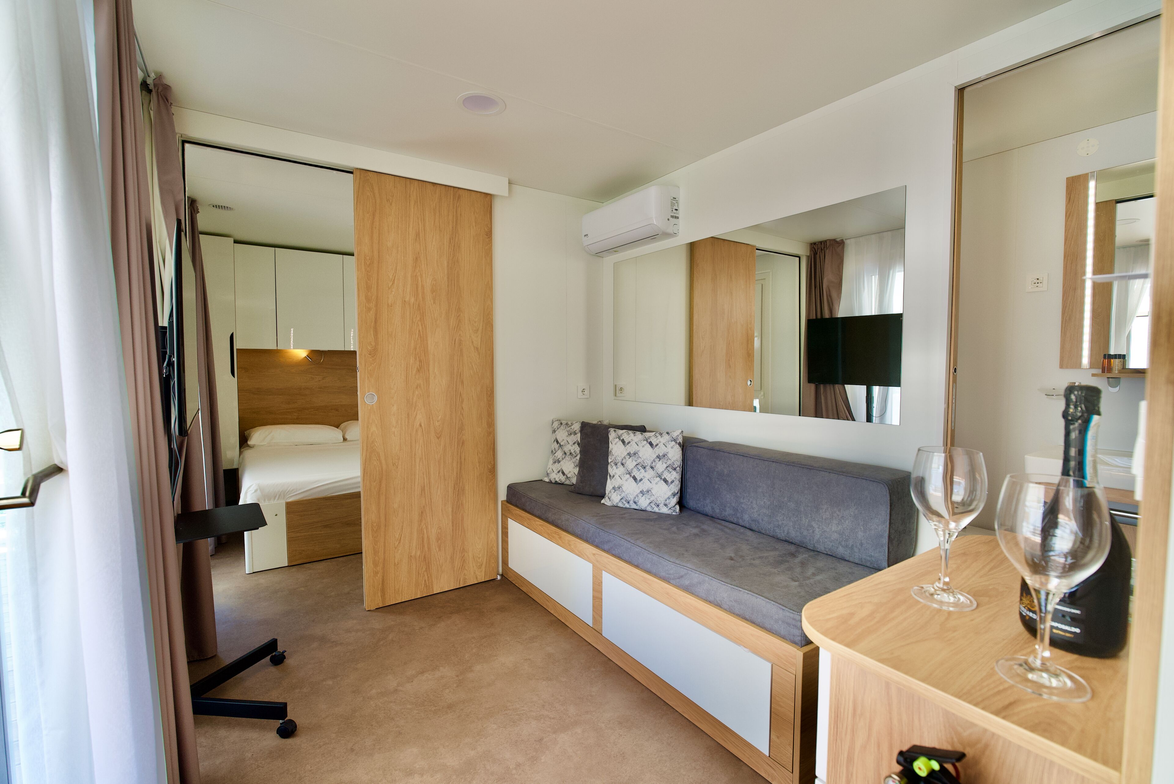 Ein modernes Hotelzimmer mit Bett, einer Couch, einem Schreibtisch mit Spiegel und einer Minibar.
