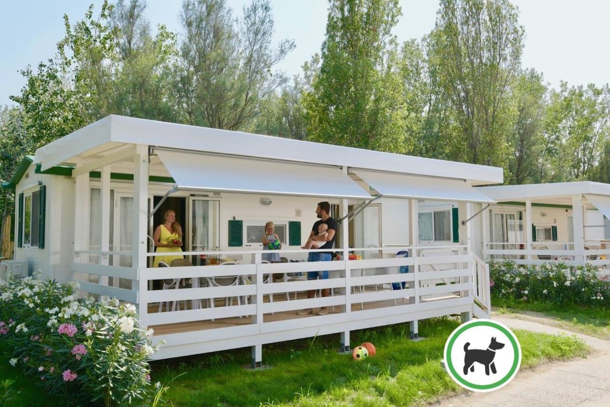 A white mobile home with a covered porch, a dining area, and a small garden.