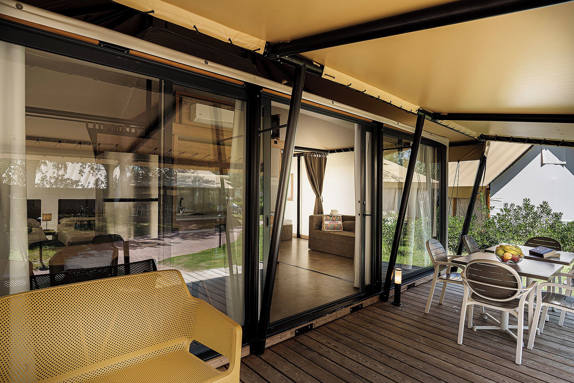 Un portico coperto con un pavimento in legno, arredi da esterno e una porta vetrata che dà su una stanza con un letto e un comodino.