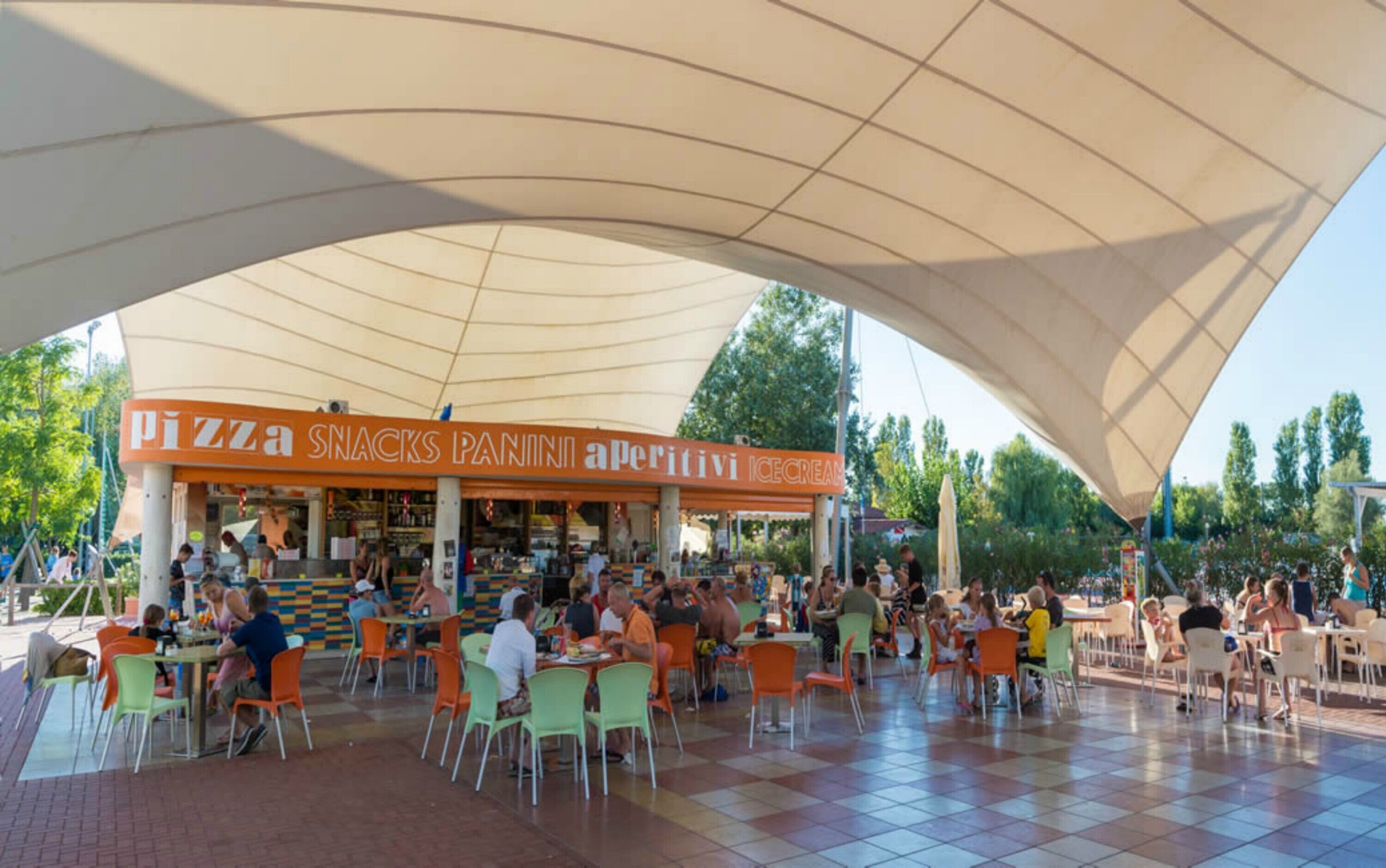 Un área de estar al aire libre con un puesto de pizza y aperitivos, rodeada por una marquesina.