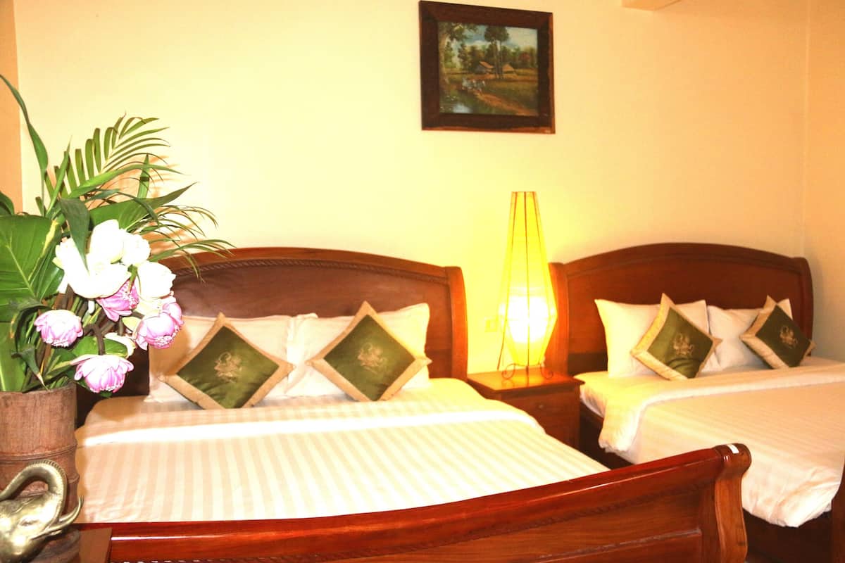 Une chambre d’hôtel avec deux lits simples, une table de chevet avec une lampe, un vase avec des fleurs et un tableau encadré au mur.