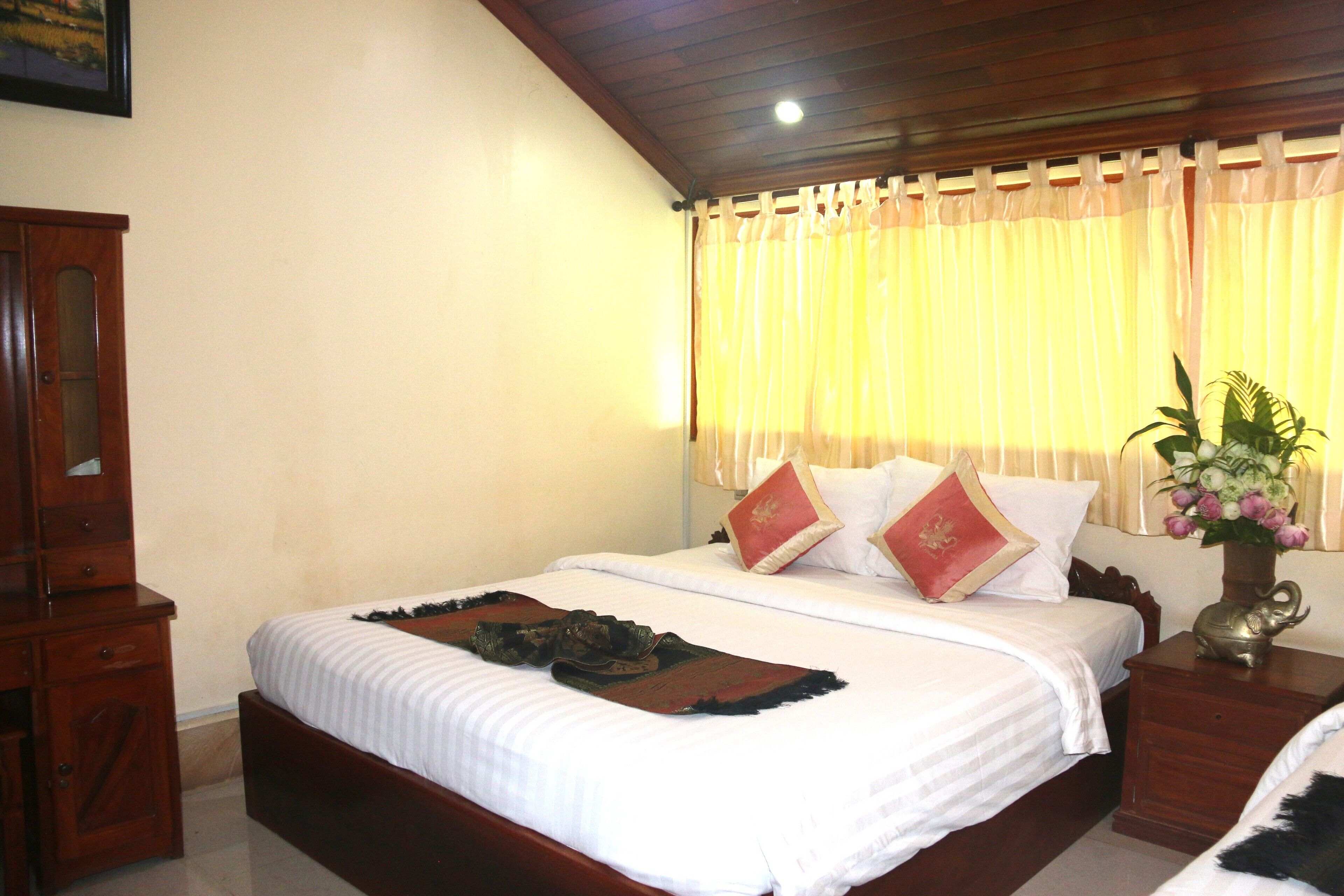 Habitación de hotel con una cama grande, cabecero de madera y mesita de noche con un jarrón de flores.