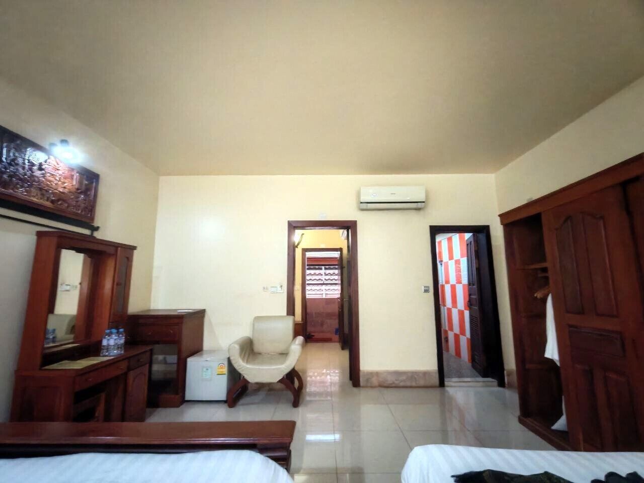 A hotel room with a bed, a desk, a chair, a wardrobe, and an air conditioning unit.
