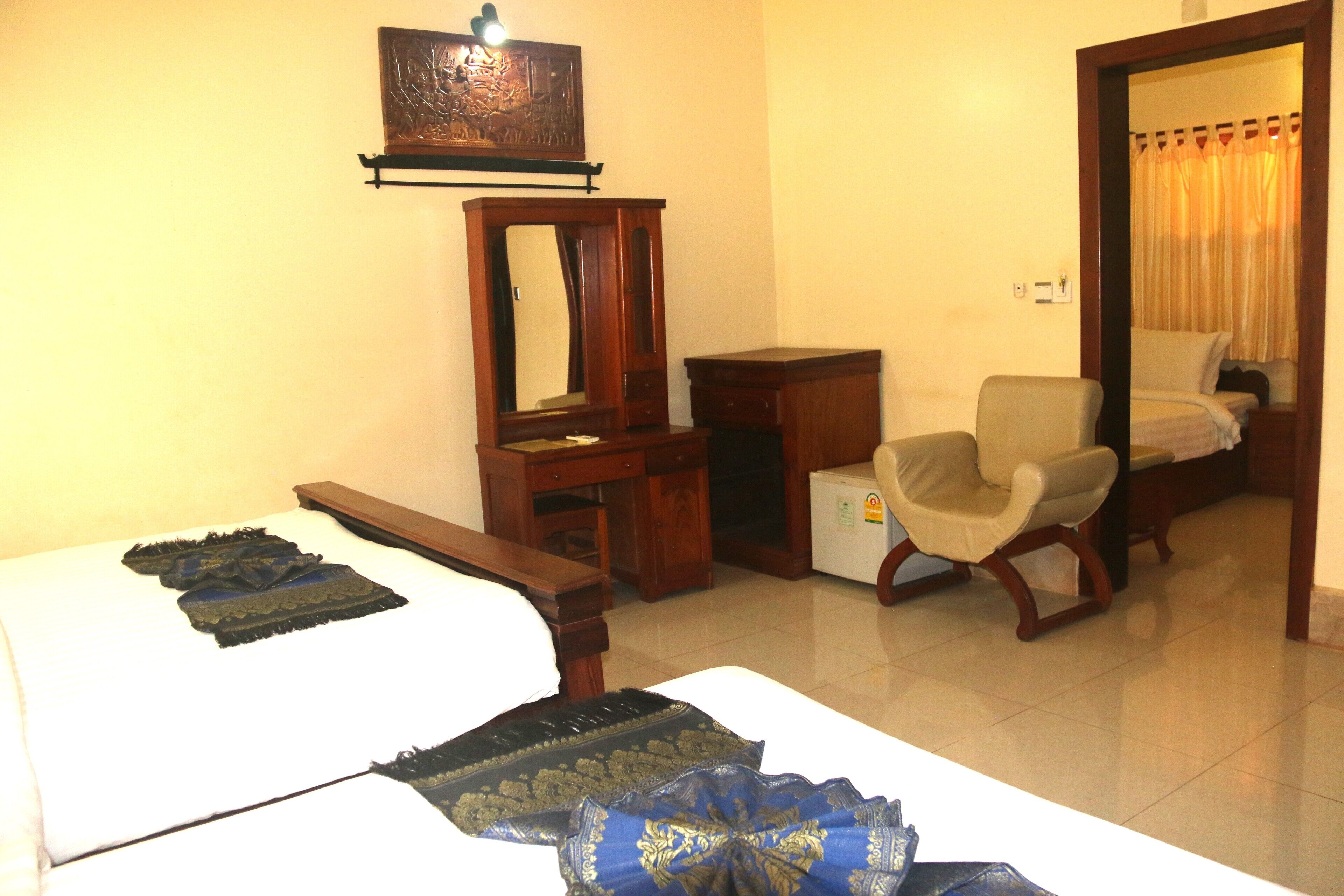A hotel room with a bed, a chair, a dresser, a mirror, and a door leading to another room.