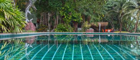 A clear blue pool with a tiled edge, surrounded by lush greenery and palm trees.