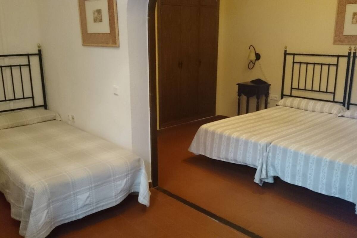 A room with two single beds, a wooden wardrobe, and a small bedside table with a lamp.