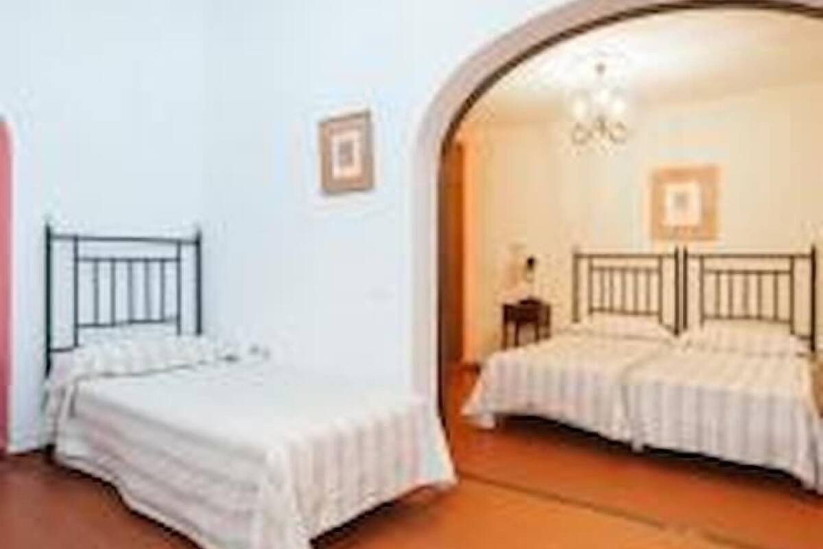 A room with two single beds, a wooden floor, and a large arched doorway leading to another room.