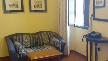 A room with a sofa, a small table, a telephone, and framed pictures on the wall.