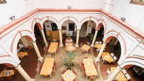 Un patio interior con varias mesas y sillas, rodeado de arcos y columnas.