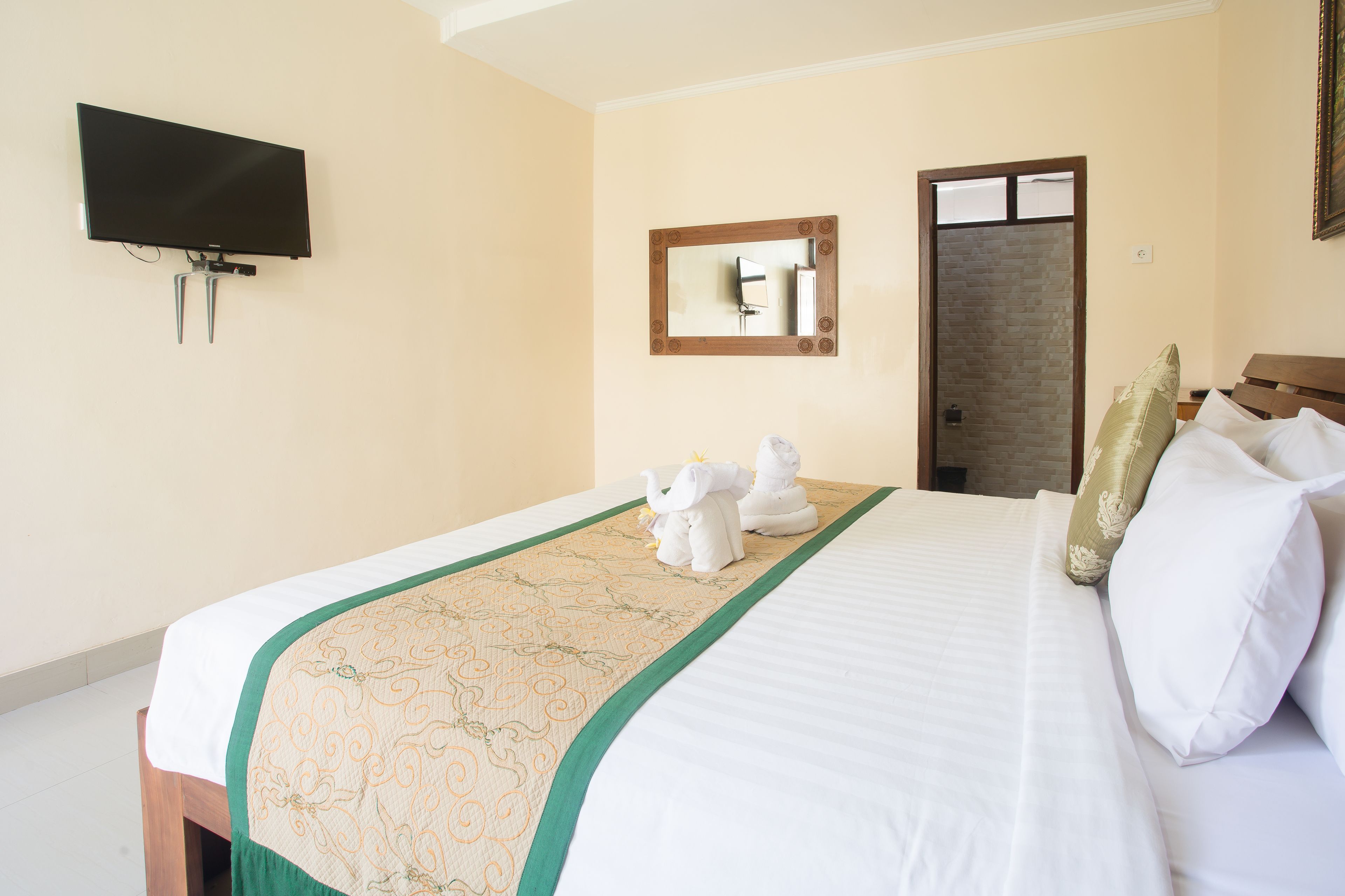 Quarto de hotel com cama, televisão de tela plana na parede, espelho e porta.