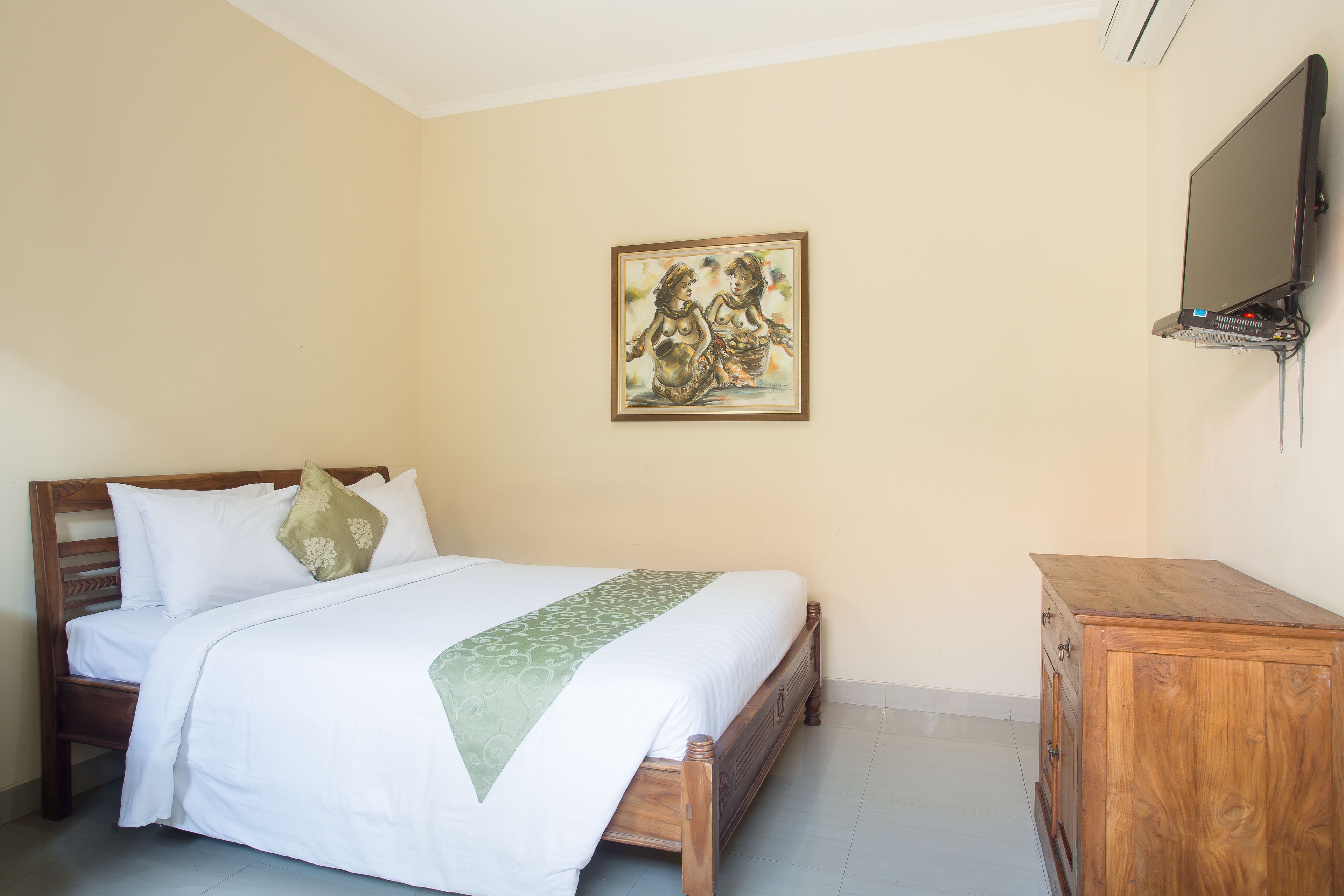 A neatly made bed with a green throw, a wooden headboard, and a wooden dresser with drawers.
