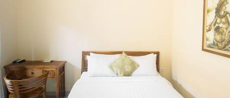 A hotel room with a wooden desk, a chair, a bed with a green patterned bedspread, and a painting on the wall.