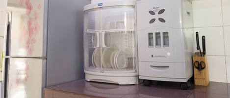 A kitchen with a refrigerator, a dish drying rack, and a cabinet with utensils.