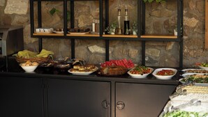 A buffet setup with various dishes and a stone wall backdrop. - Armagrandi Bozcaada (Bozcaada)