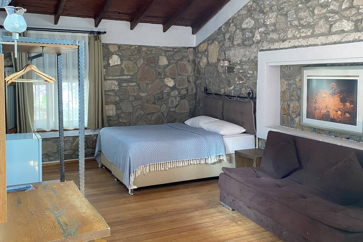 Una habitación acogedora con pared de piedra, vigas de madera en el techo, una cama, un sofá y una chimenea.