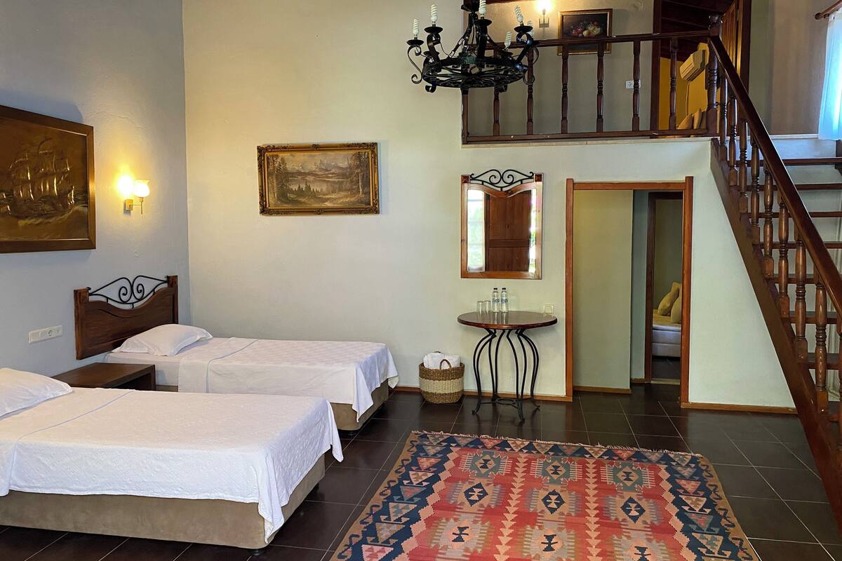 Habitación de hotel con dos camas, un candelabro, un cuadro, un espejo y una escalera.