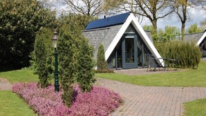 A building with a triangular roof and a paved pathway leading to it. - Bij Aquamarijn (Stieltjeskanaal)