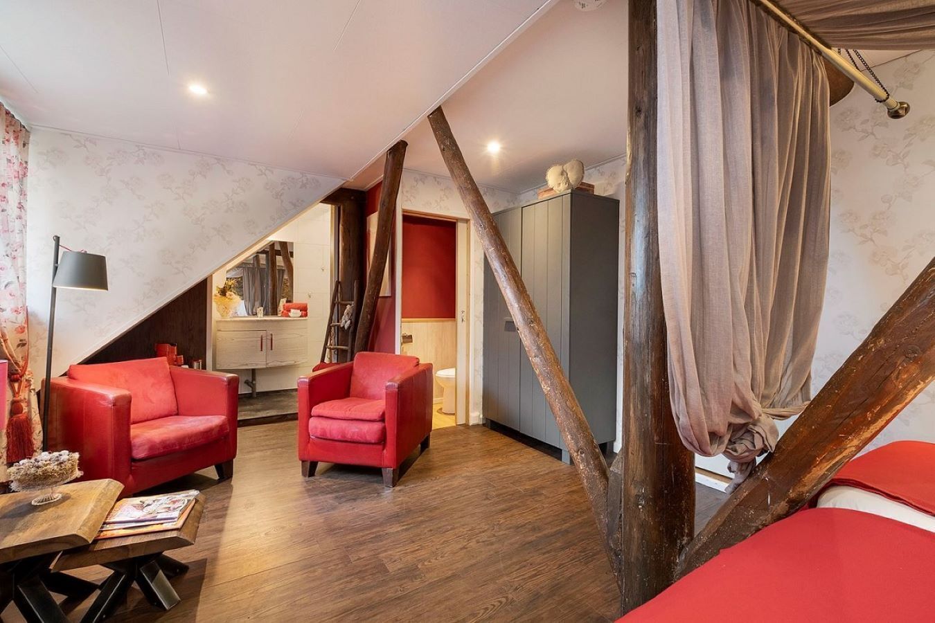 A room with a sloped ceiling, wooden beams, a red sofa, a small table, and a cabinet.