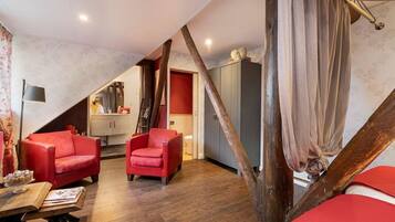 A room with a sloped ceiling, wooden beams, a red sofa, a small table, and a cabinet.