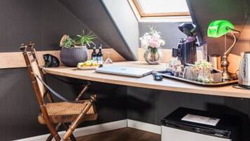 Quarto de estilo loft moderno, com teto inclinado, escrivaninha de madeira com um laptop, luminária de mesa verde e uma pequena lixeira.