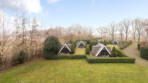 A row of small, triangular-roofed cabins with neatly trimmed hedges and a grassy lawn. - Bij Aquamarijn (Stieltjeskanaal)