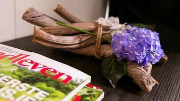Una revista titulada 'De Gelderveen' sobre una superficie de madera, junto con un manojo de ramas secas y un ramo de flores moradas.