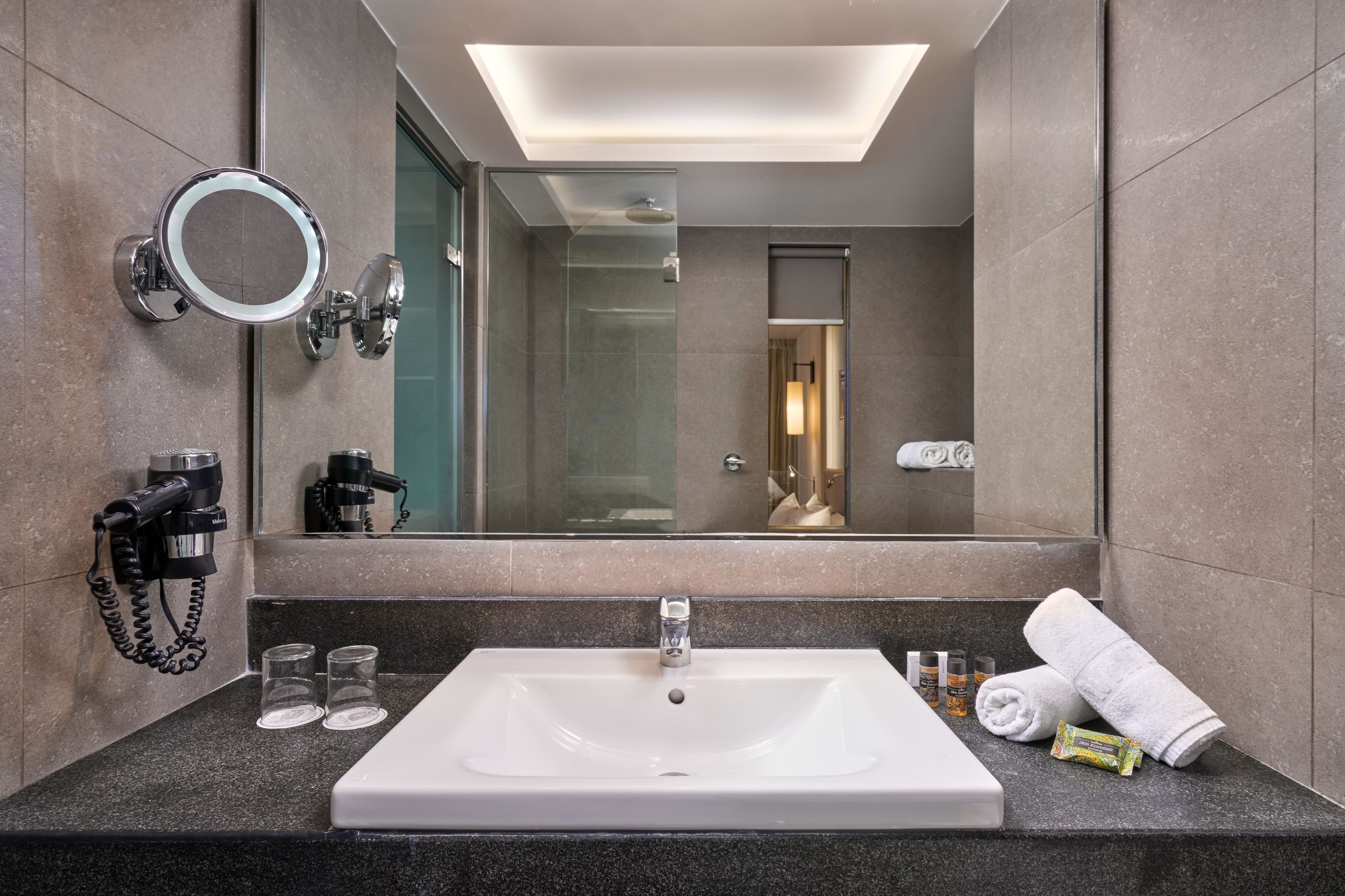 A modern bathroom with a large mirror, a sink, a hairdryer, and a towel.