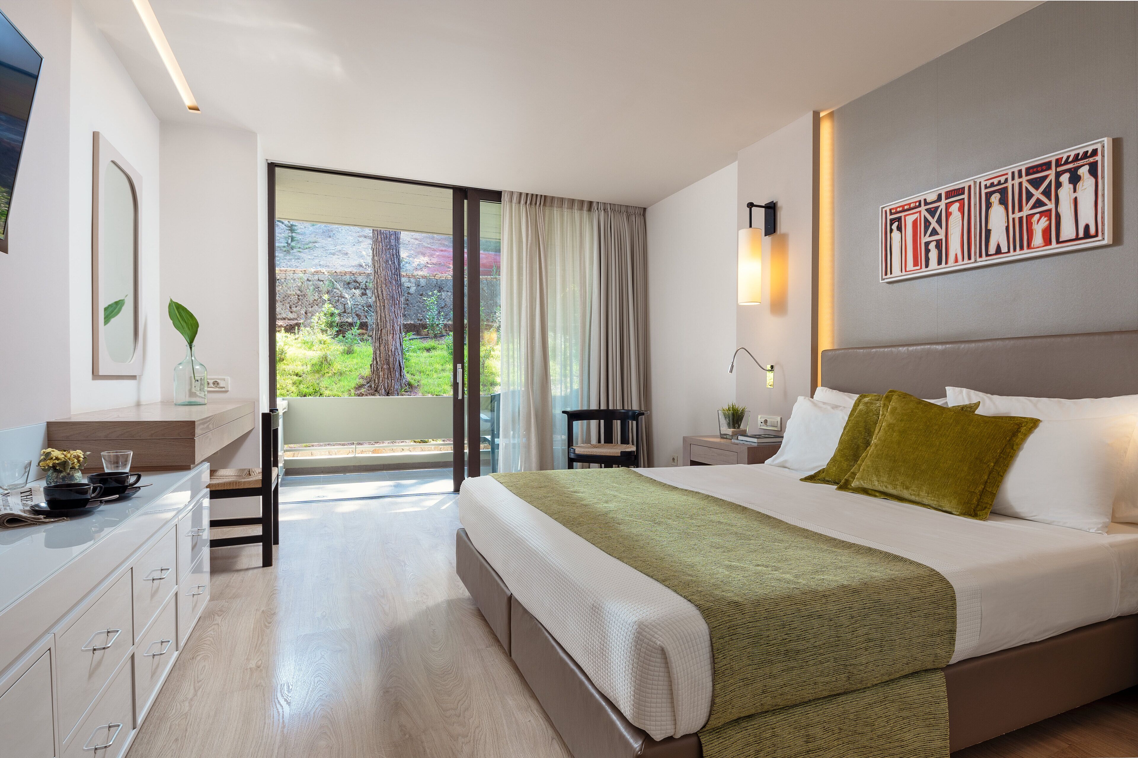 Una habitación de hotel moderna con una cama grande, un escritorio con silla, una mesita de noche y vistas al exterior.