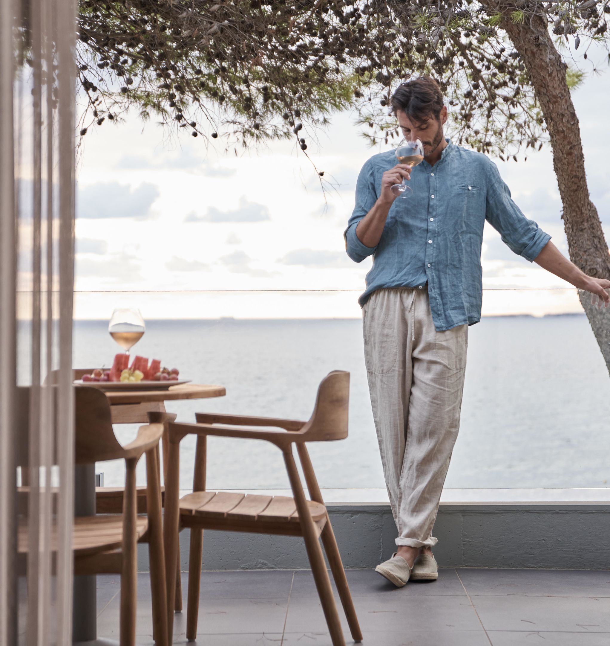 A person standing by a table with a glass of wine, overlooking a body of water.