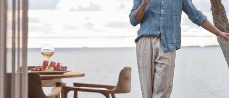 A person standing by a table with a glass of wine, overlooking a body of water.
