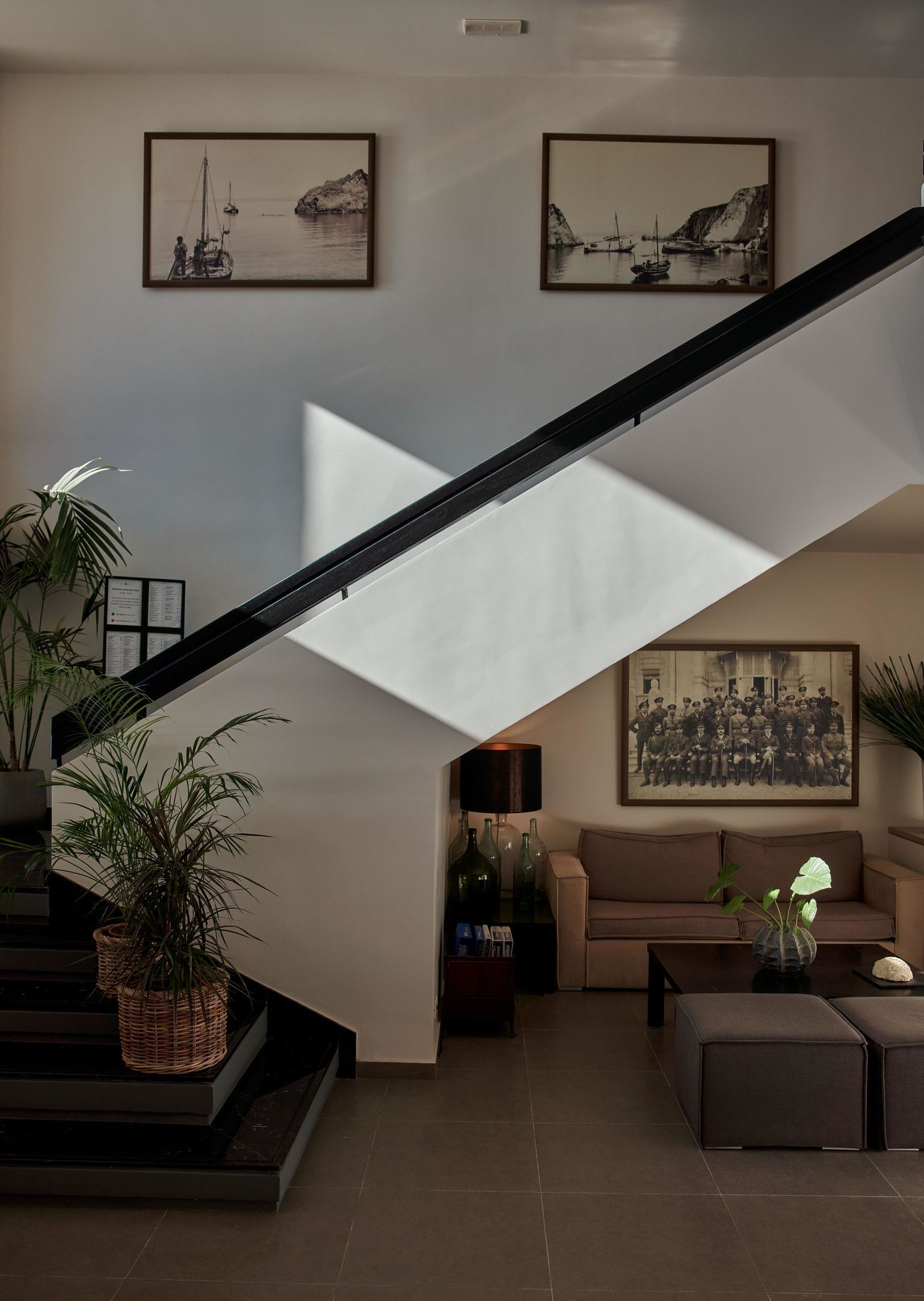 Uma sala de estar moderna com escada, um sofá, uma mesa de centro e duas pinturas em preto e branco com temática marítima.