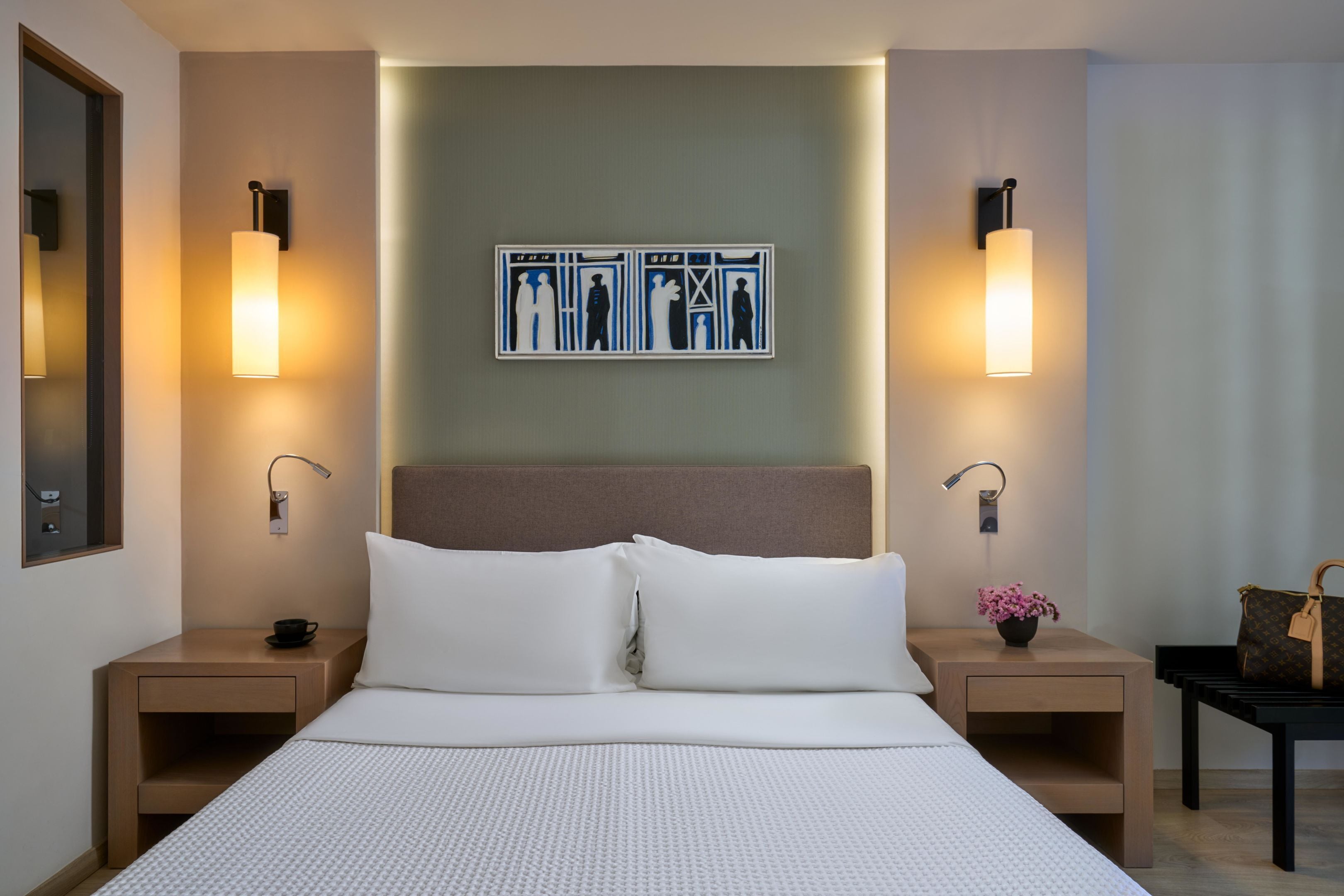 Una camera d'albergo con un letto grande, due comodini, un tavolino e un quadro appeso alla parete, più una lampada su ogni comodino.