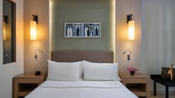 Una camera d'albergo con un letto grande, due comodini, un tavolino e un quadro appeso alla parete, più una lampada su ogni comodino.