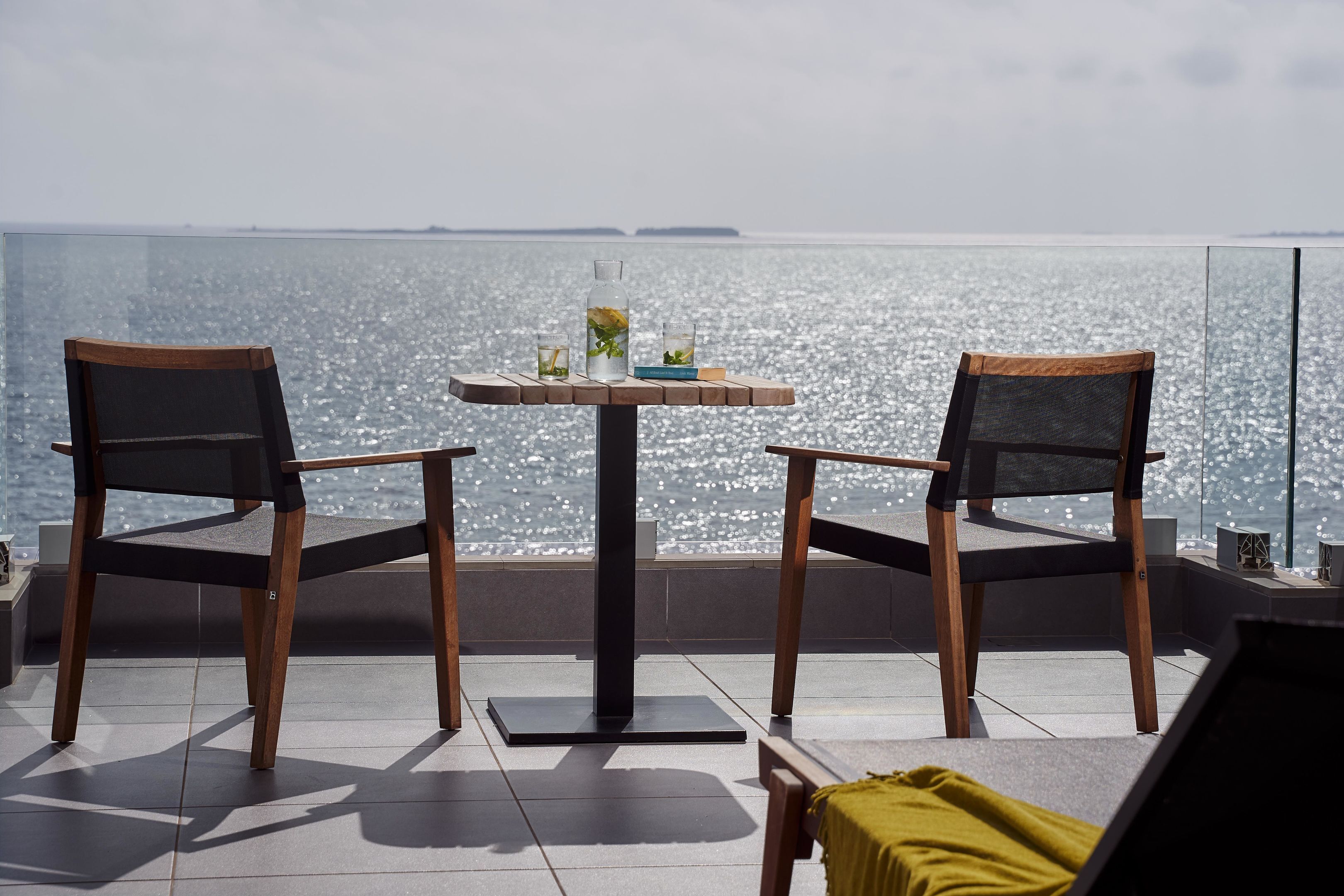 A table with two chairs facing a body of water, with a glass of water and a bottle on the table.