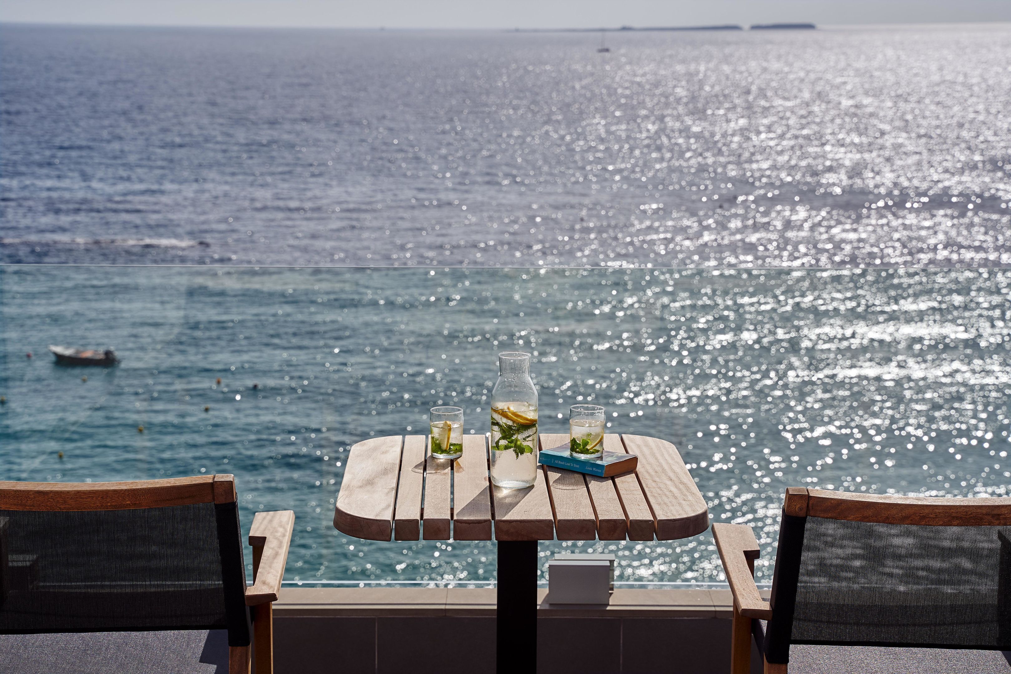 A table with a bottle and glasses, overlooking a body of water.