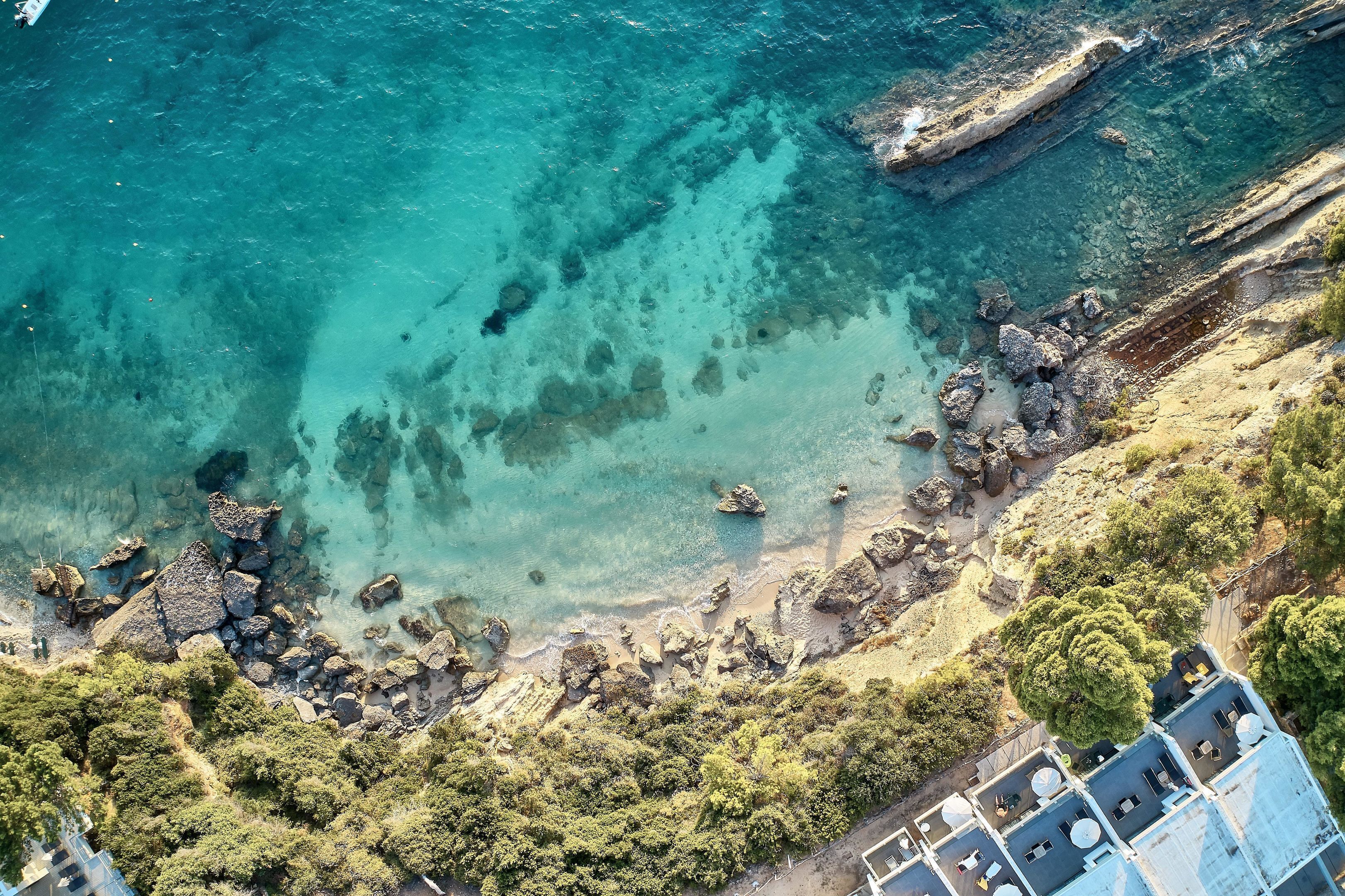 An aerial view of a coastal area with rocky terrain, clear water, and dense greenery.