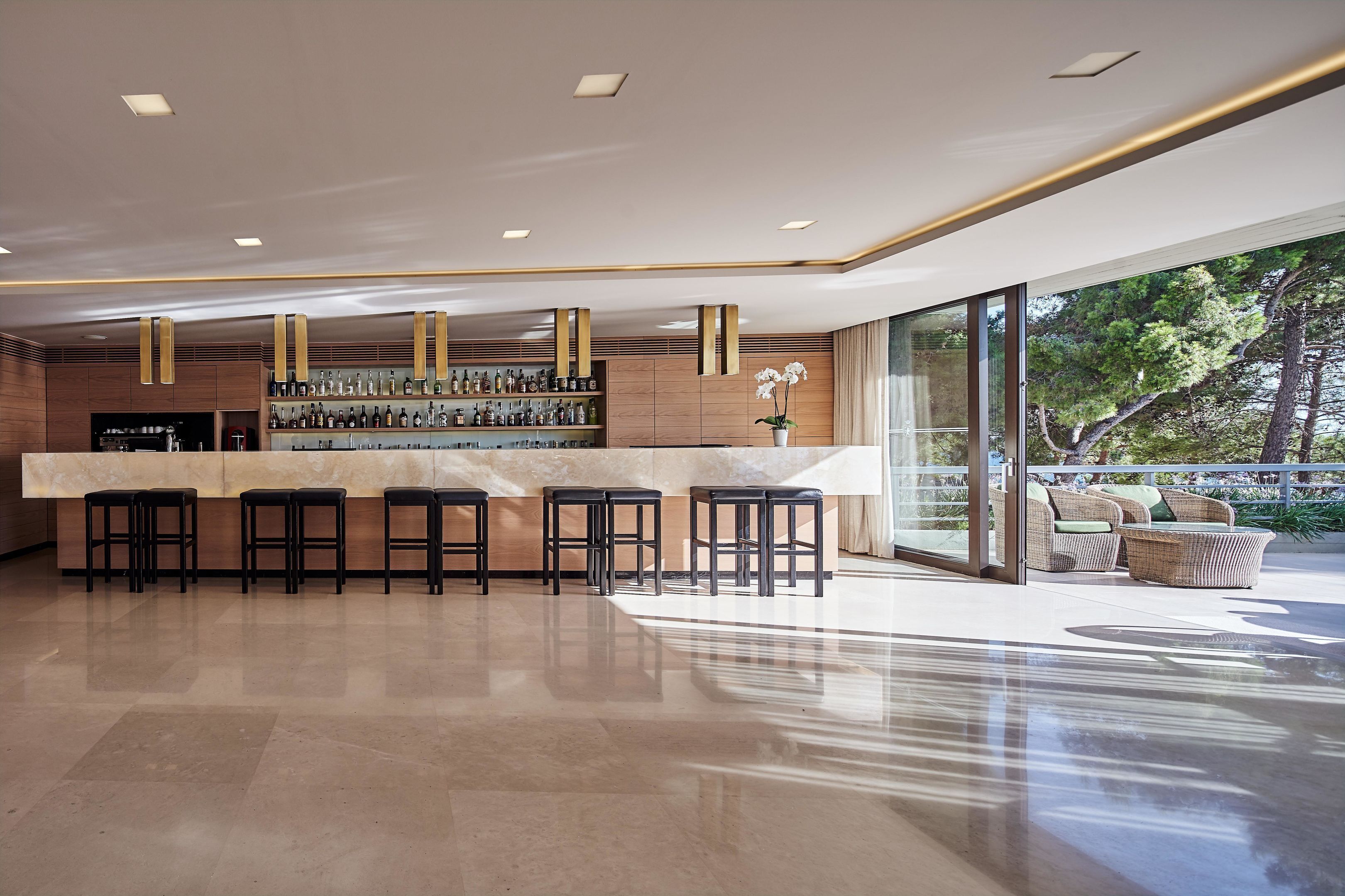 A modern bar area with a marble countertop, black stools, and a variety of bottles.