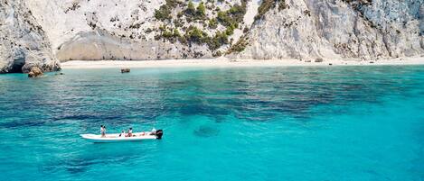 A boat on clear turquoise water with a rocky coastline and cliffs in the background.