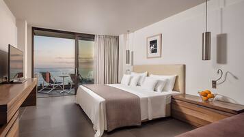 A modern hotel room with a bed, a desk, a chair, and a view of the sea.