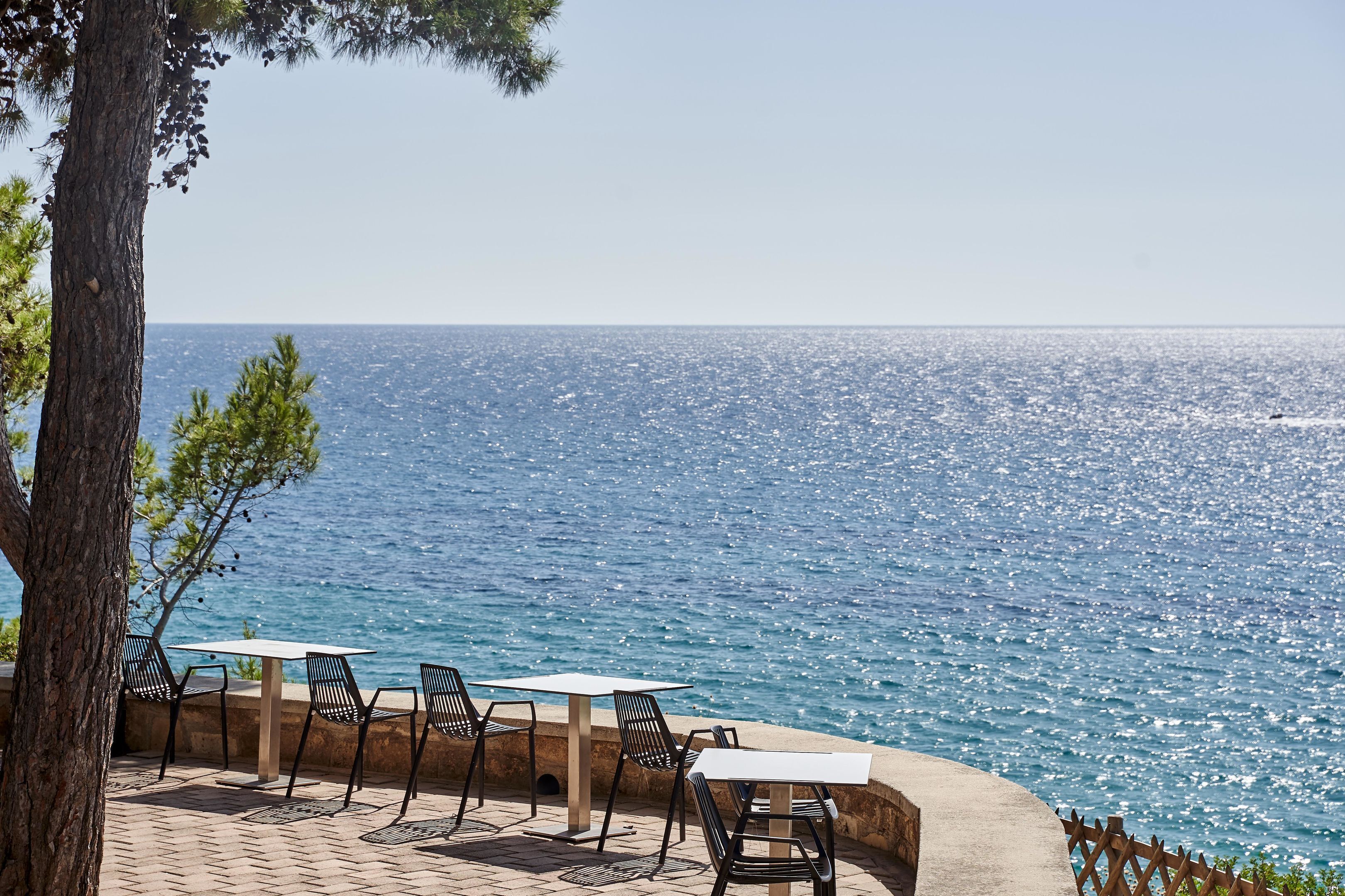 An outdoor seating area with tables and chairs facing a body of water.
