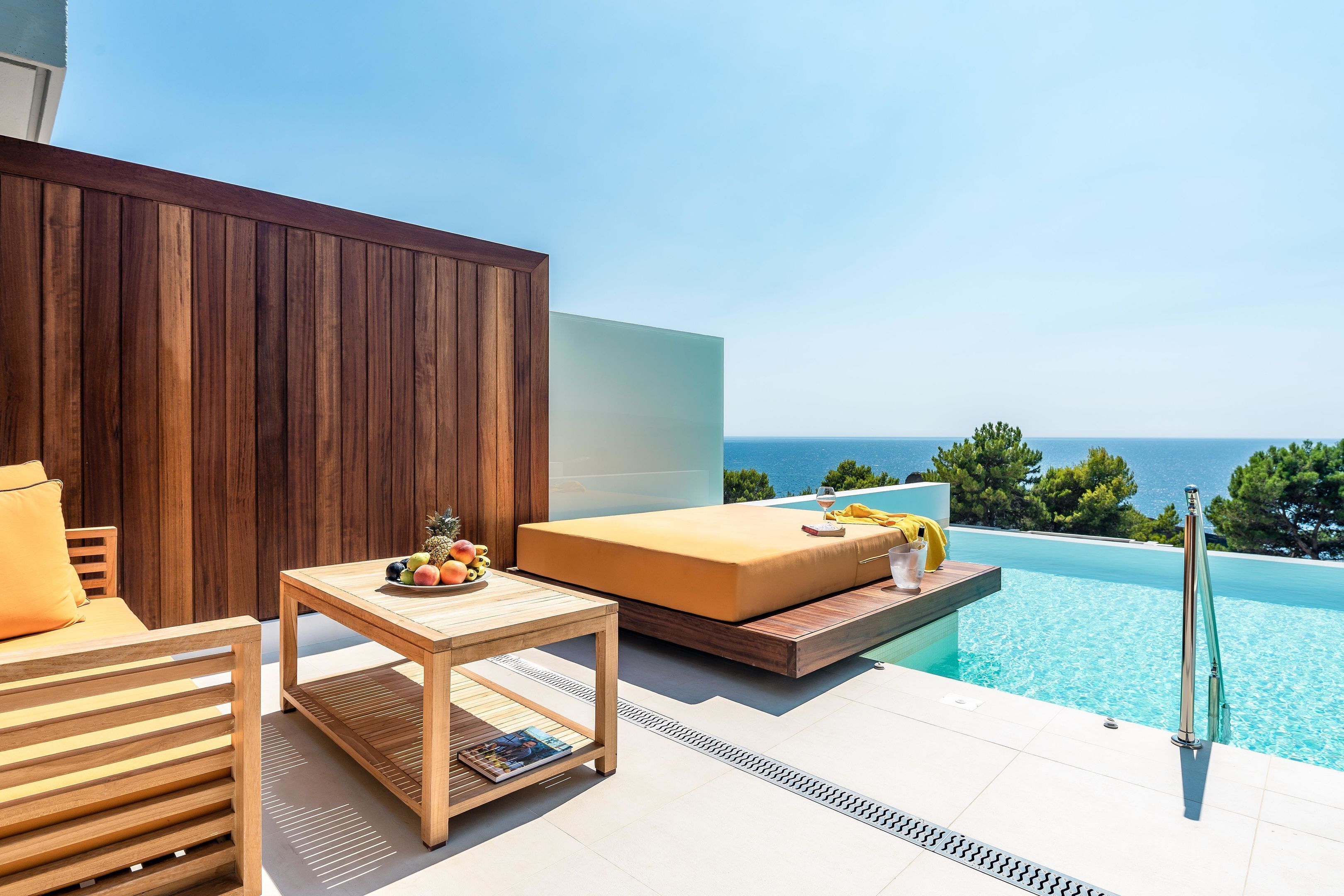 A modern outdoor seating area with a wooden table, a cushioned bench, and a poolside view.