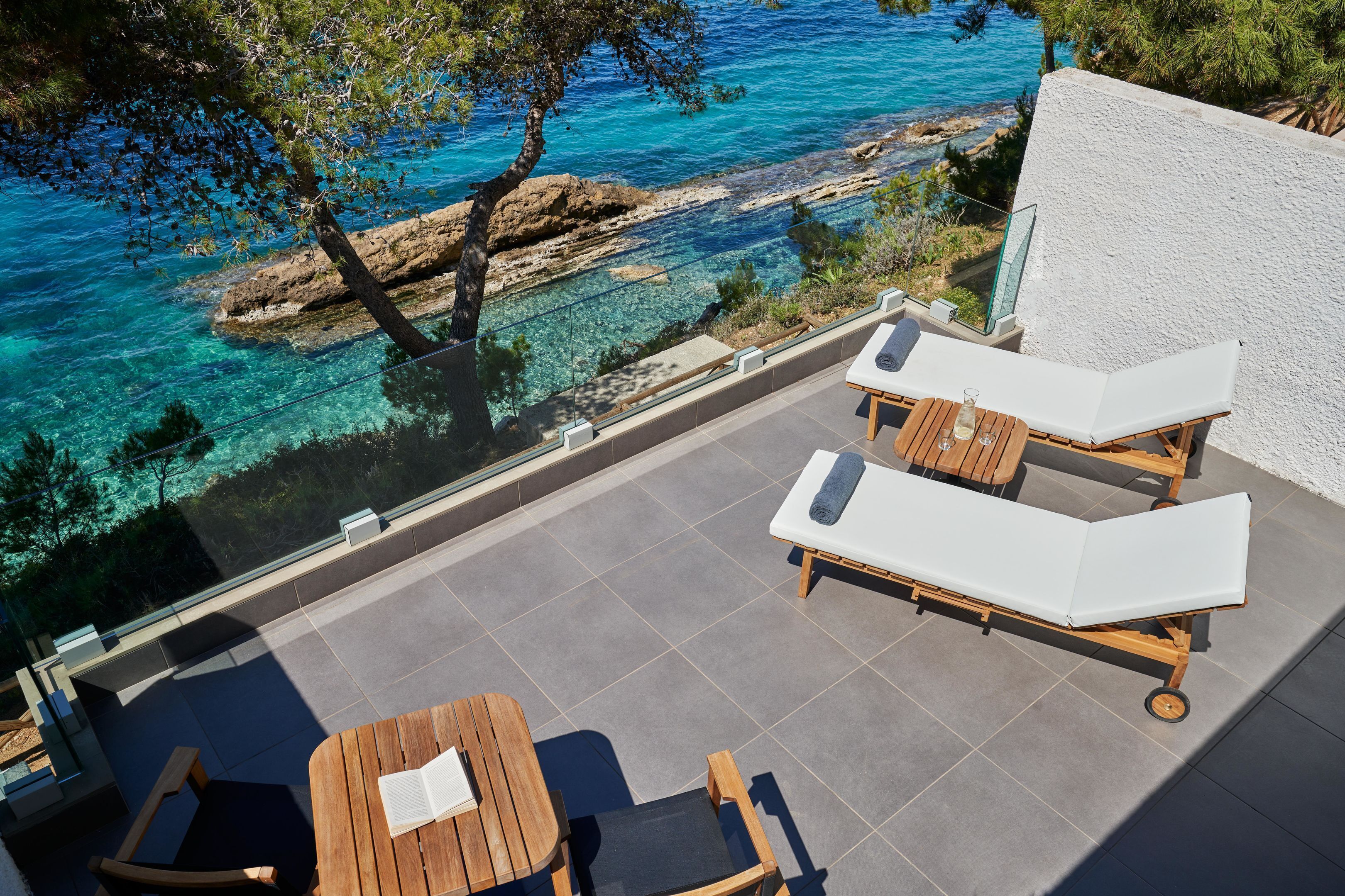 A terrace with two lounge chairs, a table, and a view of the sea.